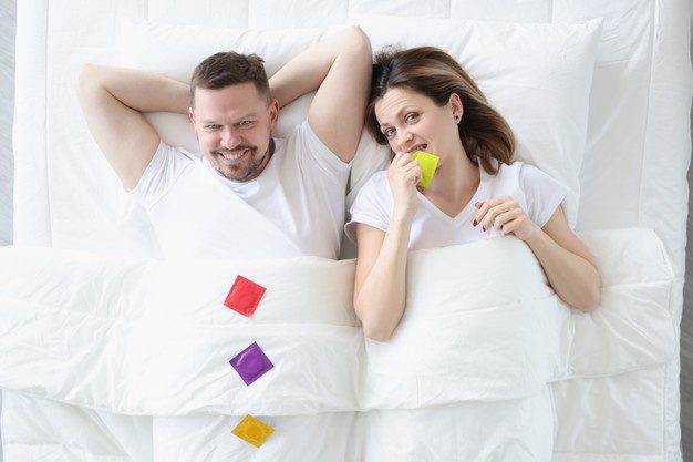 yatakta uzanan çiftler ve ellerinde renkli prezervatifler