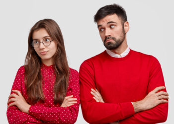 Jealous girlfriend turns from boyfriend, feels offended after sorting out relationships, keeps hands crossed, bearded male looks with pity expression, asks for forgiveness. Relations concept