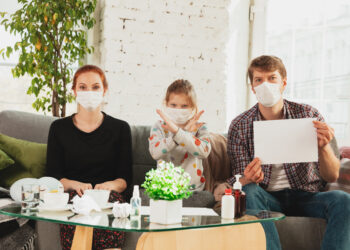 Caucasian famiy in face masks and gloves isolated at home with coronavirus respiratory symptoms such as fever, headache, cough in mild condition. Healthcare, medicine, quarantine, treatment concept.